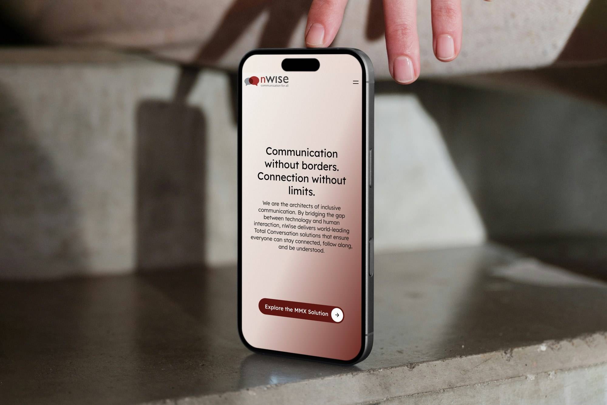 A hand setting an iPhone down on a concrete ledge, showing the nWise homepage headed 'Communication without borders. Connection without limits.'