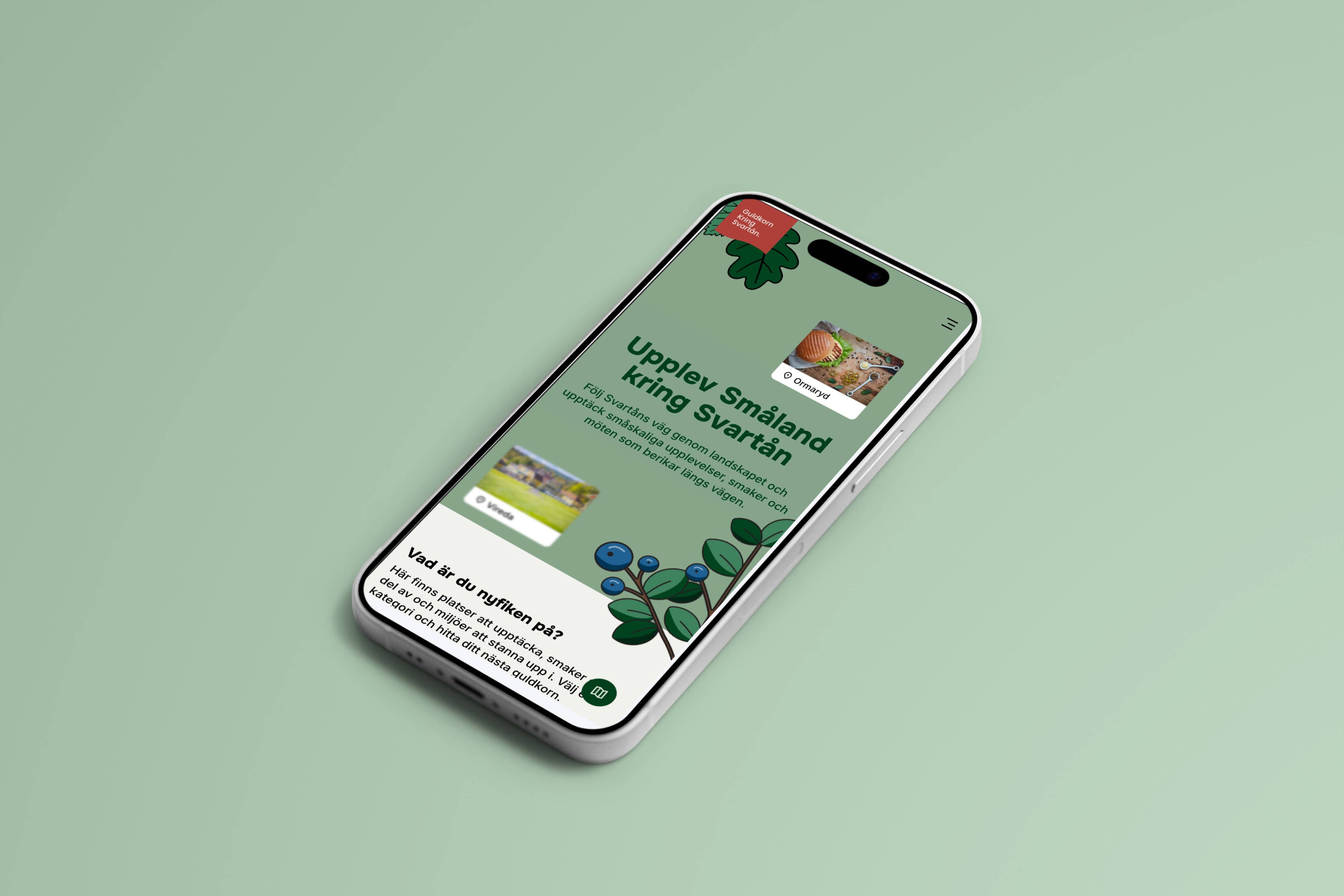 The same homepage on a phone lying on a sage-green surface, with photo cards tagged Ormaryd and Vireda, the illustrated blueberry sprig, and the round map button in the bottom corner.